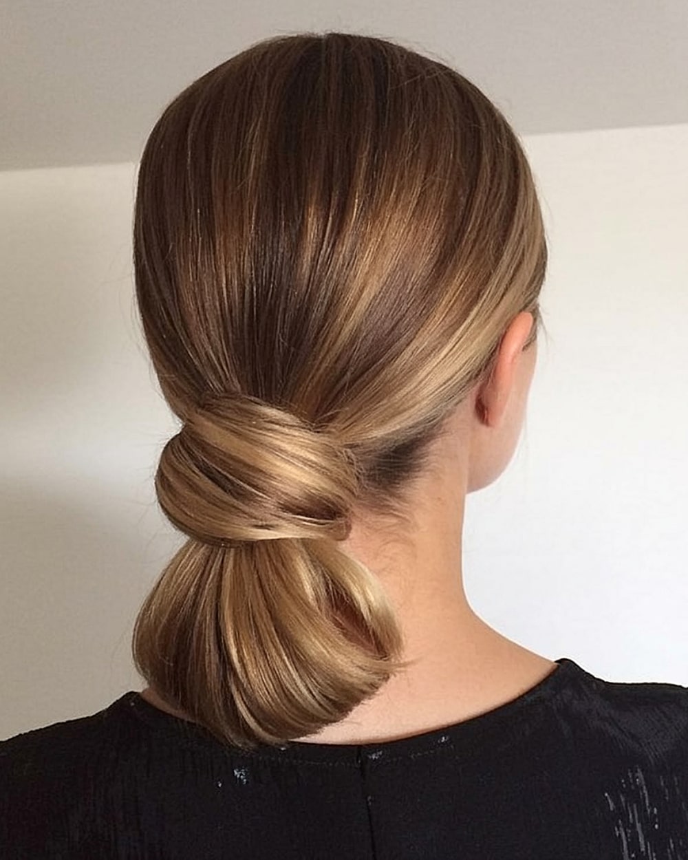 Low looped ponytail bun on smooth caramel-blonde hair, an easy updo for sleek everyday styling